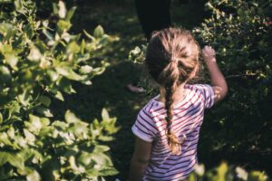 Young girl with braided hair enjoying a sunny day outdoors in a lush green garden.